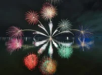 夜空の花火が水面に色鮮やかに映るイメージ