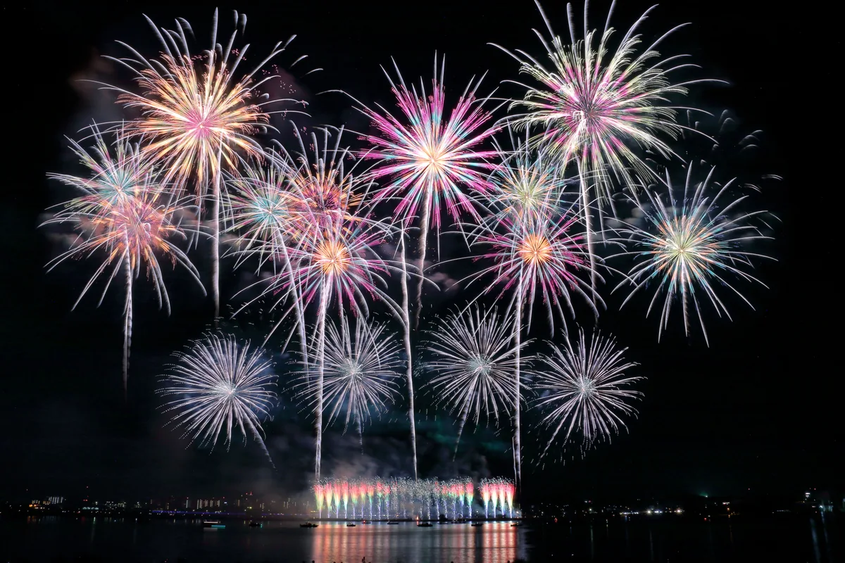 水辺の夜空に複数の花火が上がるイメージ
