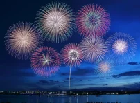 水辺の夜空に複数のカラフルな花火が上がるイメージ