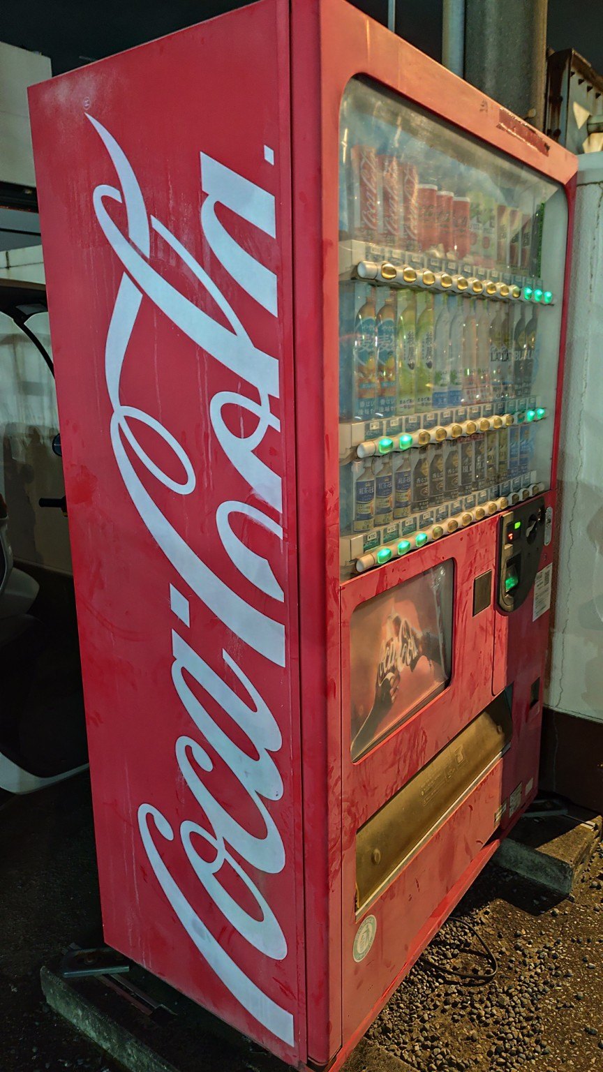 駐車場にある赤色が色あせたコカ・コーラの自動販売機